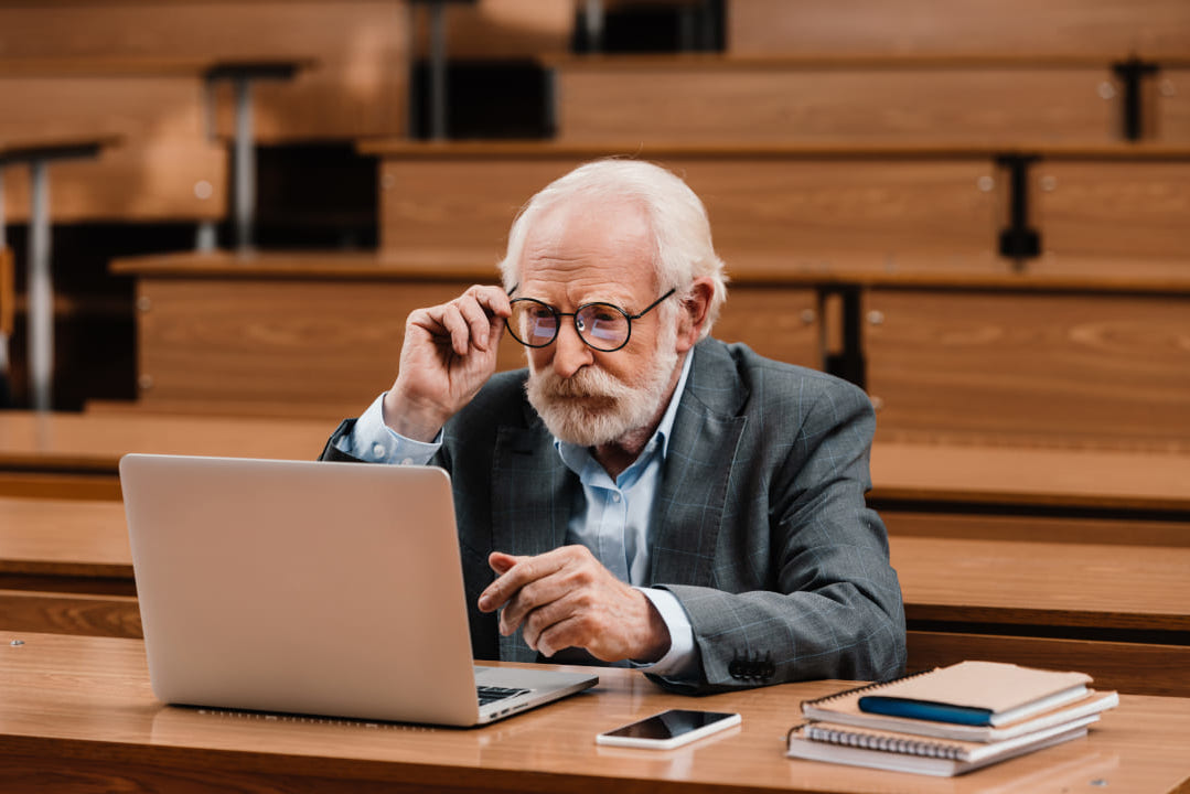 Old veteran university researcher reading laptop learning about transcriptions for university